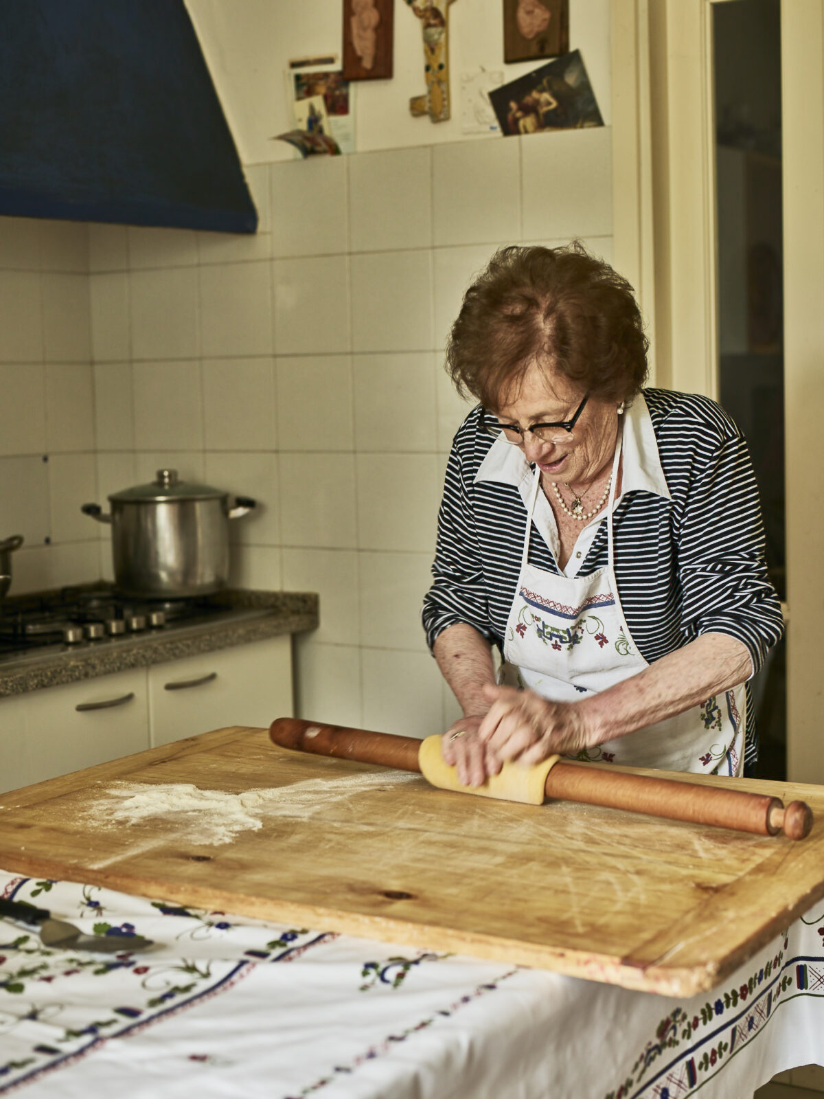 One of the pasta grannies rolling pasta dough on a dining table with tablecloth in a kitchen