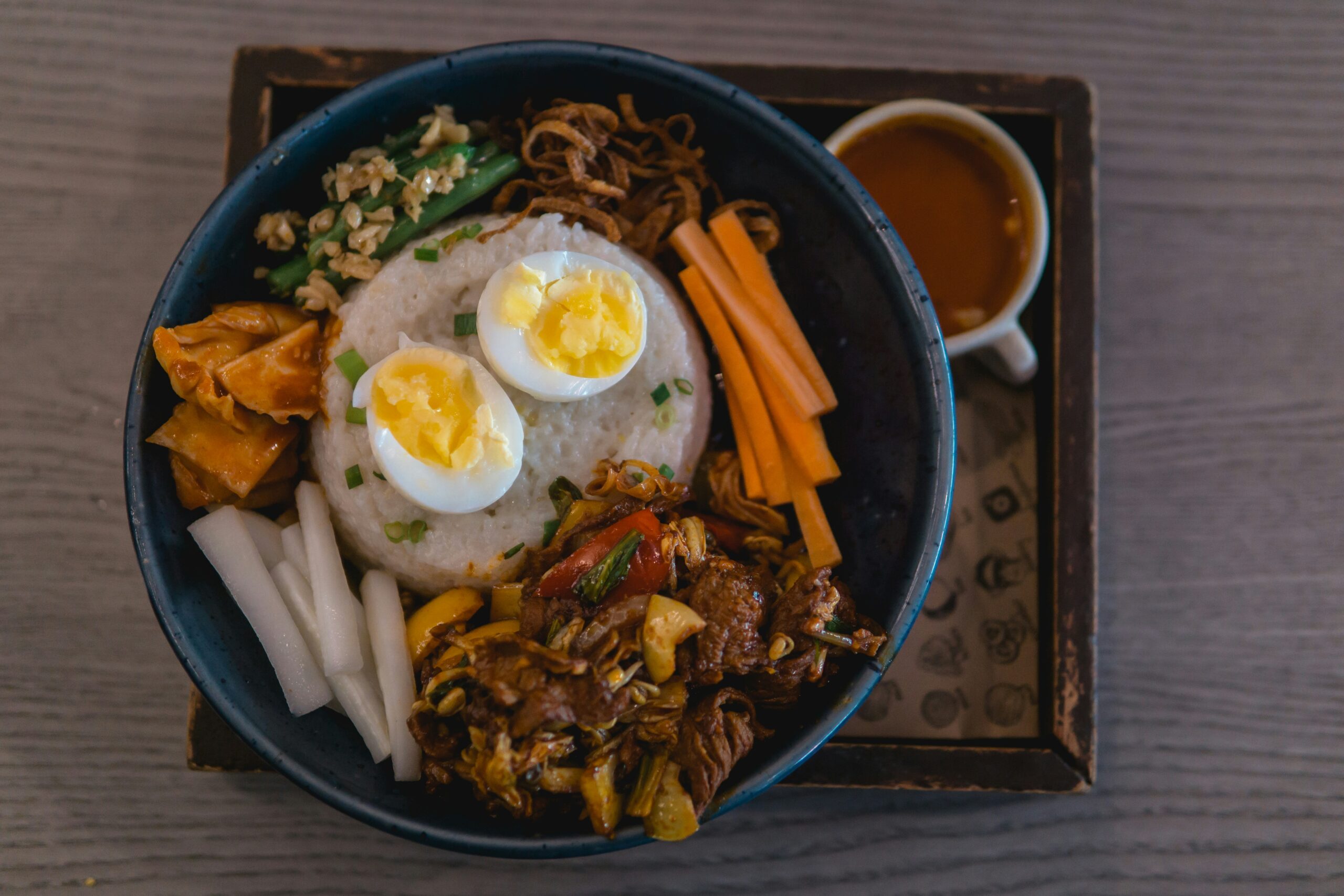 Beef bibimbap with a boiled egg and kimchi in a blue bowl on a tray with a cup of tea